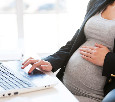 Cropped image of pregnant businesswoman typing something on laptop while sitting at her working place in office